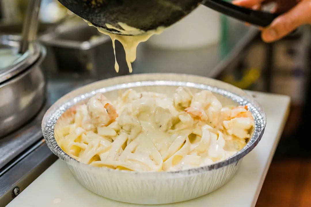 Cream sauce poured over pasta in a takeaway tray